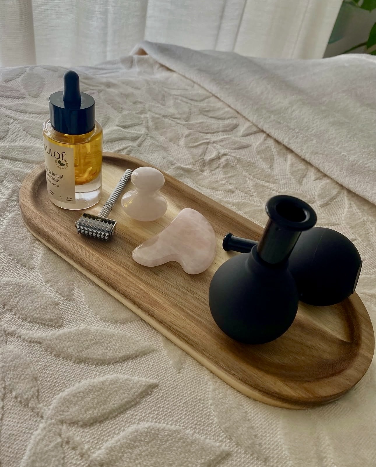 Herramientas de masaje facial —ventosas, gua-sha, rodillo y aceite— sobre una bandeja de madera