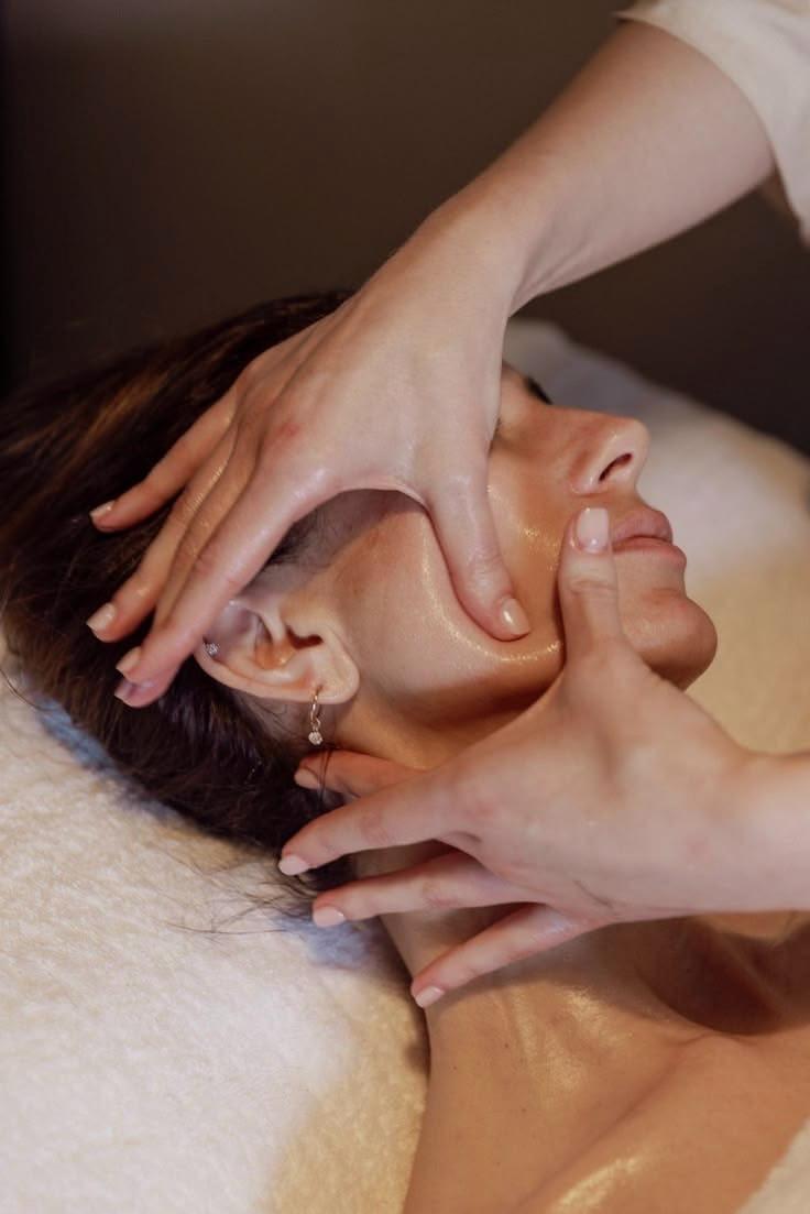 Manos de una profesional realizando un masaje facial a una clienta con la piel luminosa