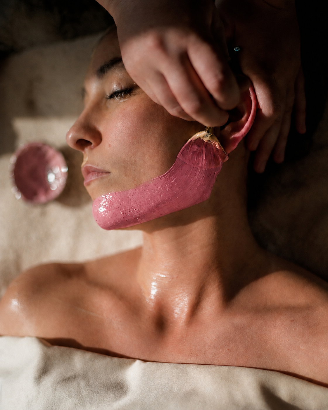 Aplicación profesional de una mascarilla rosa a lo largo del rostro de perfil